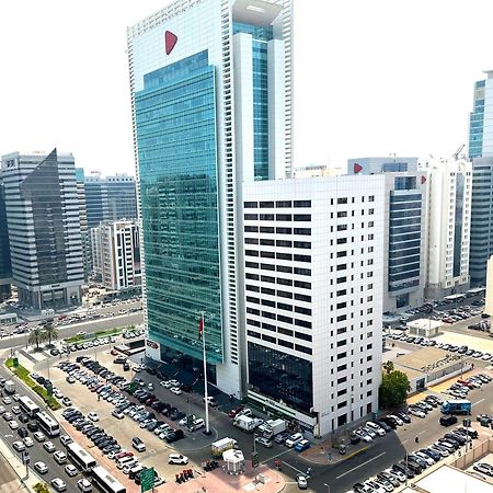 Royal Rose Abu Dhabi, A Curio Collection By Hilton Affiliated Hotel Exterior photo The photo depicts a modern urban scene featuring a cluster of skyscrapers. In the foreground, there is a prominent glass building with a distinct corporate design, displaying a large logo at the top. Surrounding it are other tall buildings with varyi