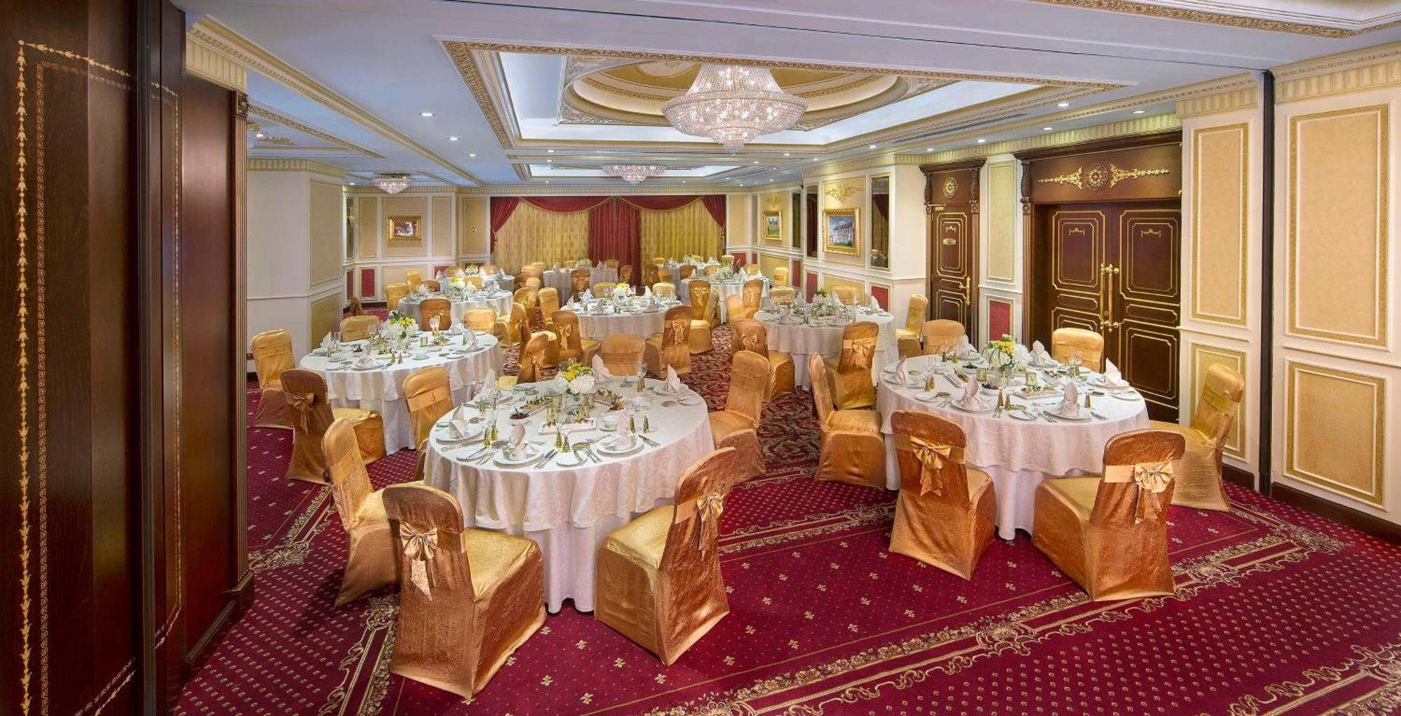 Royal Rose Abu Dhabi, A Curio Collection By Hilton Affiliated Hotel Exterior photo The photo shows an elegantly arranged banquet hall set up for a formal event. There are several round tables covered with white tablecloths, each adorned with gold or cream-colored chair covers that match the upscale decor. The tables are set with fi