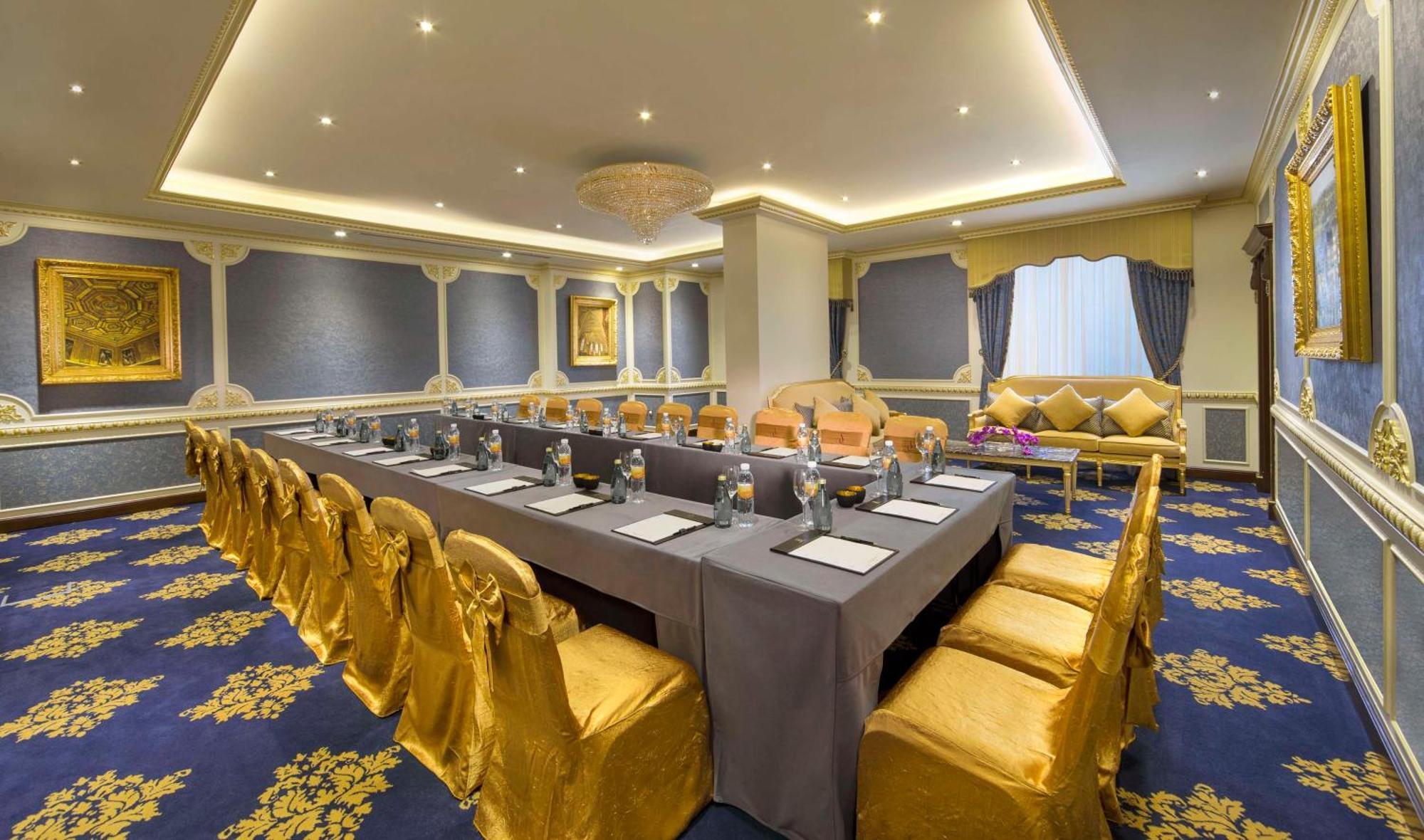 Royal Rose Abu Dhabi, A Curio Collection By Hilton Affiliated Hotel Exterior photo The photo displays an elegantly decorated meeting room. It features a long table set for a formal gathering, surrounded by gold-draped chairs. The table is covered with a gray tablecloth, and each place setting includes a placemat or menu. The room h