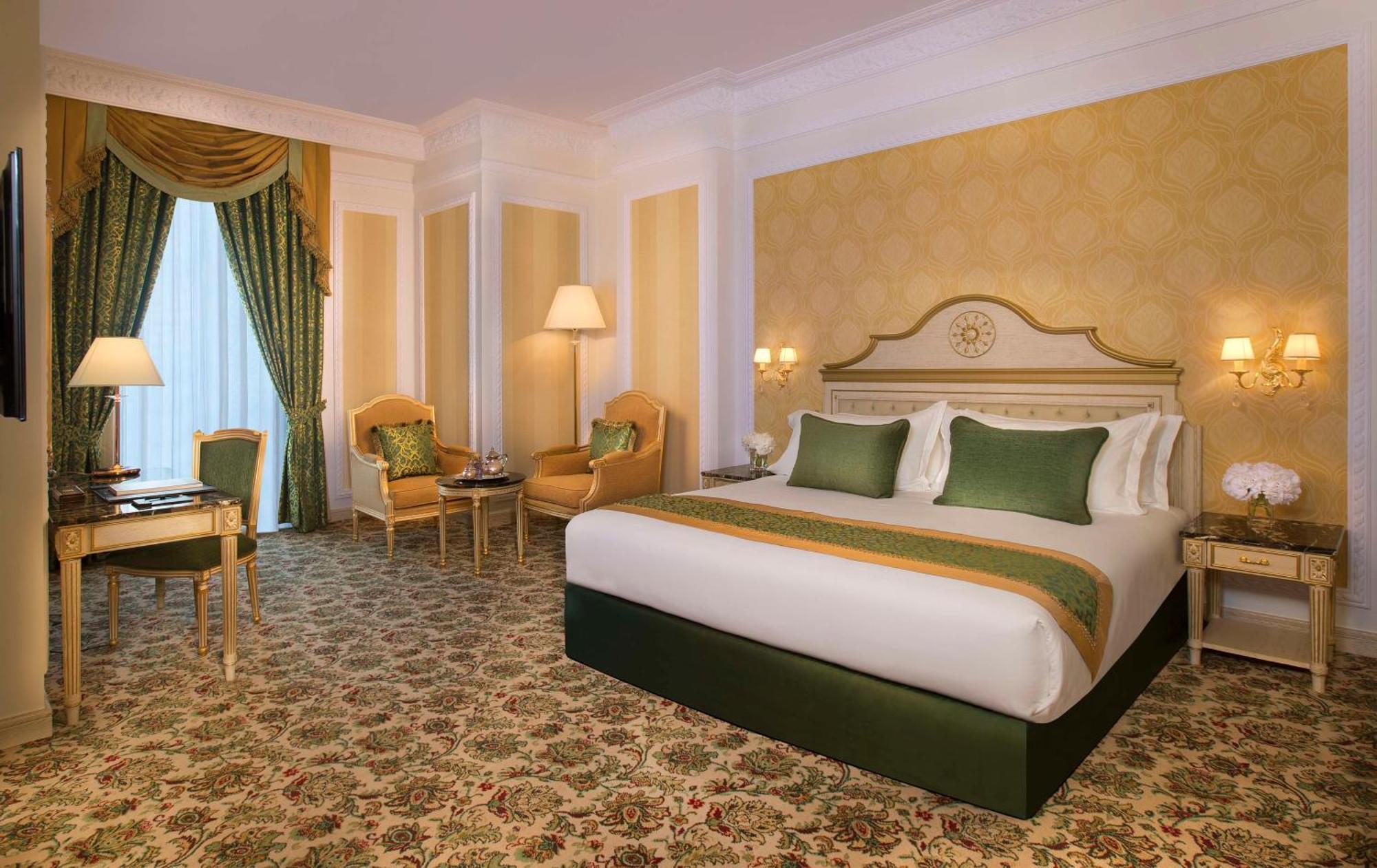 Royal Rose Abu Dhabi, A Curio Collection By Hilton Affiliated Hotel Exterior photo The photo shows a luxurious hotel room featuring elegant decor. It has a large bed with plush white bedding accented by green decorative pillows. The room is adorned with soft, golden-colored wallpaper and has a plush carpet with intricate patterns. 