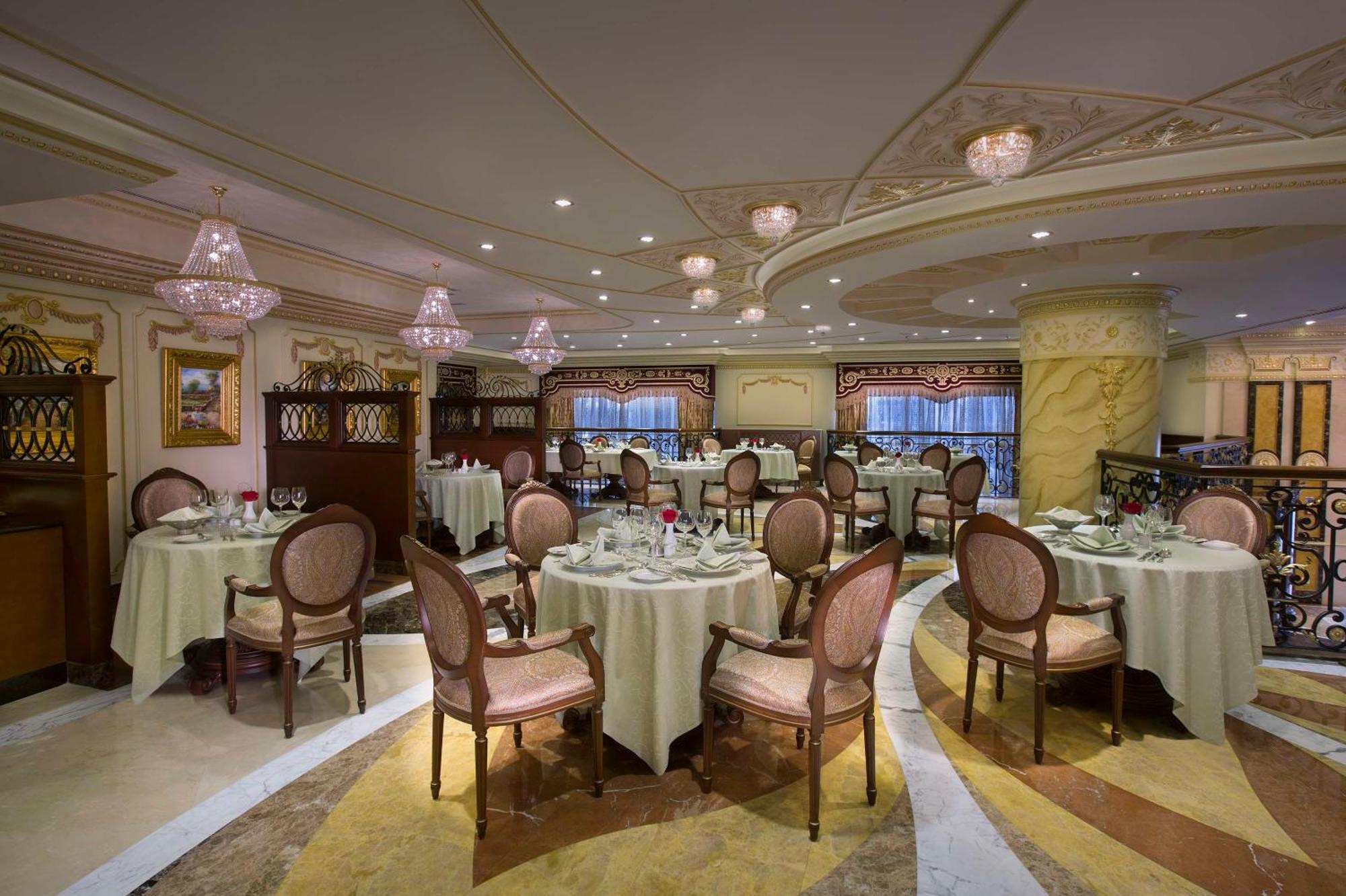 Royal Rose Abu Dhabi, A Curio Collection By Hilton Affiliated Hotel Exterior photo The photo shows an elegantly decorated restaurant interior. The space features round tables covered with white tablecloths, each set with cutlery and glassware. Stylish, upholstered chairs surround the tables. The lighting is soft, with decorative ch
