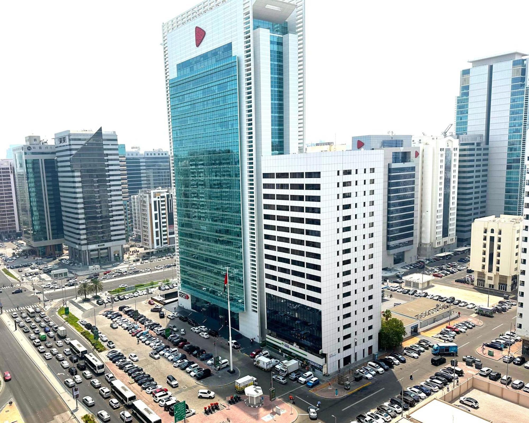 Royal Rose Abu Dhabi, A Curio Collection By Hilton Affiliated Hotel Exterior photo The photo depicts a modern urban scene featuring a cluster of skyscrapers. In the foreground, there is a prominent glass building with a distinct corporate design, displaying a large logo at the top. Surrounding it are other tall buildings with varyi